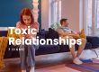 7 Toxic Relationship Signs - featured image. A couple sitting on a blue sofa with a yellow throw blanket, The man is on the far right, looing out through a glass door and the woman on the left, busy on her phone.