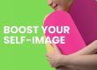 Featured article image. White writing says, boost your self-image. Neon green background and foreground with woman in yellow top hugging a two tone large pink heart.